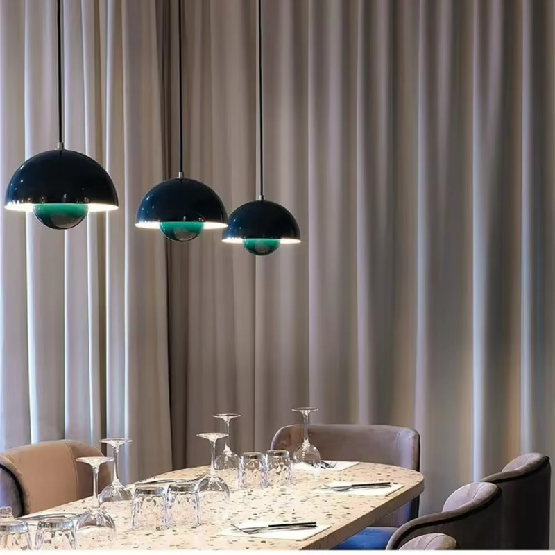 Dining table set with wine glasses and cutlery under three pendant lights against a curtain backdrop.