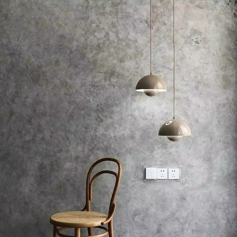 Two pendant lights hanging from a gray concrete wall with a wooden chair in the foreground.